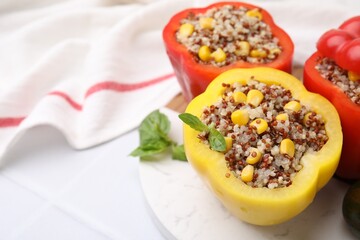 Quinoa stuffed bell peppers and basil on white tiled table, closeup. Space for text