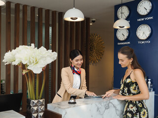 Young travelers talking and check-in register information with woman receptionist worker standing in counter hotel reception counter desk at lobby modern hotel..