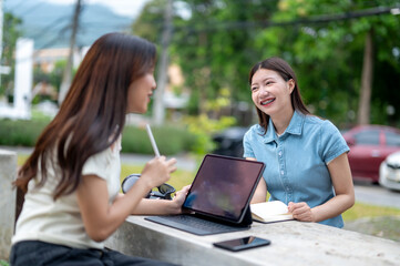 Two women sitting at a table with a laptop and a book