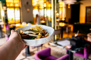 Close-up of a hand presenting a gourmet dish in a well-lit, cozy restaurant setting with modern...