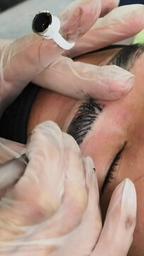 An esthetician using a microblade tool to make small cuts into the eyebrow of a customer. A Microblading technique to implant pigment. Male brow enhancement.