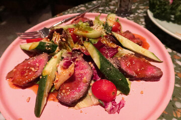 close up of slow cook beef steak with cucumber cherry tomato salad on a pink plate with dressing