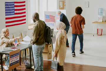 High angle view wide shot of diverse citizens taking ballot papers and voting at polling station on election day, copy space