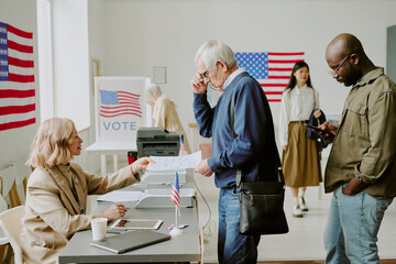 Side view shot of senior Caucasian man attending polling place taking ballot paper to vote on election day