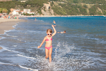 Happy child on sea beach. Kid running in waves. Little girl having fun, enjoying summer vacation, resort. Concept of travel, carefree childhood, tourism. Lifestyle authentic moment