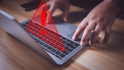 Hacker or programmer using laptop with triangle caution warning sign, coding, cryptography, hacker, crime, virus, for notification error and maintenance concept. Computer with red warning sign.