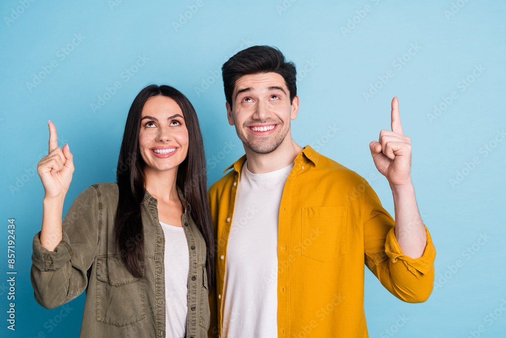 Poster Photo of two nice young partners look point fingers up empty space wear shirt isolated on blue color background