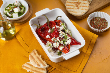 Grilled red pepper with feta cheese and olive oil on white tray on yellow background.