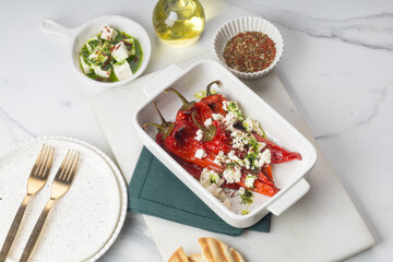 Grilled red pepper with feta cheese and olive oil on white tray on yellow background.