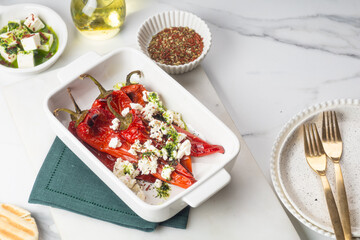 Grilled red pepper with feta cheese and olive oil on white tray on yellow background.