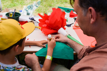 Father and son are engaged in creativity together. Dad spends time with his son cutting out large red flowers from paper