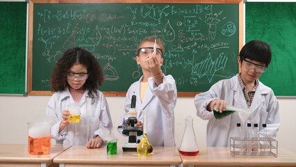 Children doing experiment in science lesson while standing at blackboard at laboratory. Happy student discovering and learning about biochemical liquid while inspecting and mixing sample. Pedagogy.