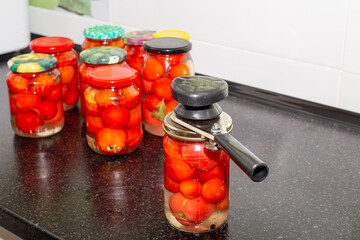 Red ripe tomatoes in glass jars and a mechanical capper. Preparing vegetables for the winter