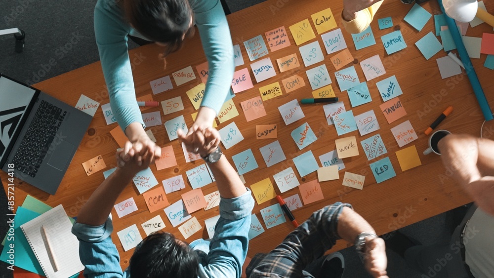 Poster top view of business team giving high five to celebrate project while standing at table with sticky 