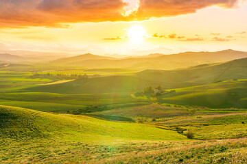 spring season green landscape of green field and meadow in a hill countryside with mountains and beautiful sunset sky on background