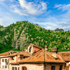 Obraz premium landscape of beautiful vintage houses with orange tile roofs in vintage venetian style to amazing high green mountain with ancient buildings on slopes and nice cloudy sky on background
