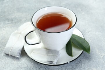 Aromatic tea in cup, teabags and green leaves on grey table