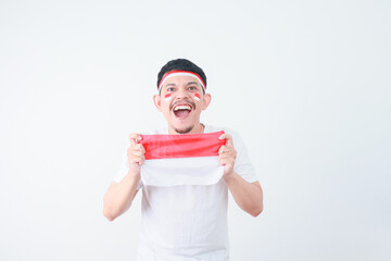 Excited young Asian man celebrate Indonesian independence day on 17 August by holding the Indonesian flag isolated over white background