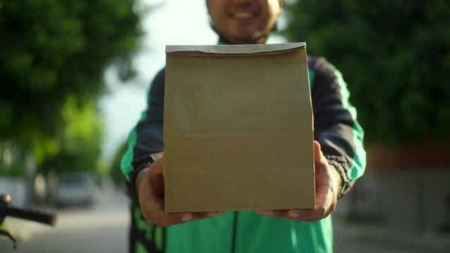Paper bag on hand Rider food delivery man cycling a bicycle the food service to customer. Happy delivery man with green backpack shipping of goods to customers.
