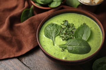 Delicious spinach cream soup with fresh leaves and microgreens in bowl on wooden table, closeup
