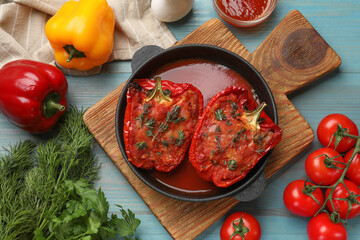 Tasty stuffed peppers in dish and ingredients on light blue wooden table, flat lay