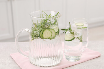 Refreshing cucumber water with rosemary on table in kitchen, closeup