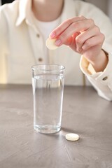 Woman putting effervescent pill into glass of water at grey table, closeup