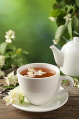 Aromatic jasmine tea in cup, flowers, green leaves and teapot on wooden table outdoors