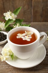 Aromatic jasmine tea in cup, flowers and green leaves on wooden table