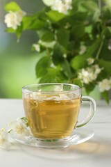 Aromatic jasmine tea in cup, flowers and green leaves on white table