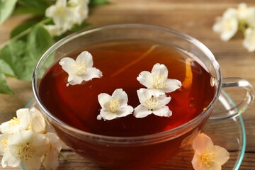 Hot jasmine tea in cup and flowers on wooden table, closeup