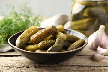 Pickled cucumbers in bowl on wooden table, closeup