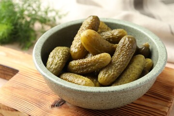Pickled cucumbers in bowl on wooden board, closeup