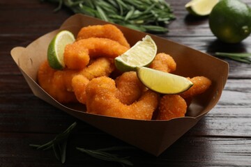 Delicious breaded fried shrimps, lime and rosemary on wooden table