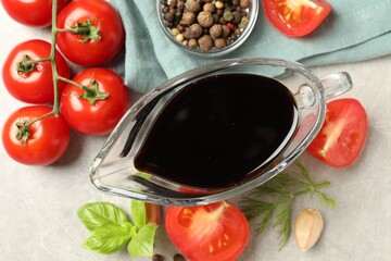 Balsamic vinegar in gravy boat, tomatoes, herbs and spices on gray textured table, flat lay