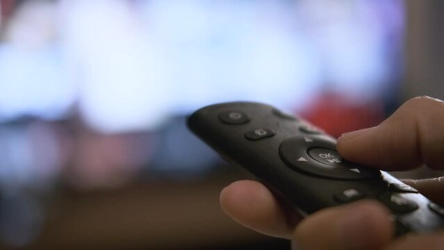 woman's hand who is pressing the TV remote to select a show or movie to watch on the streaming platform After returning from work in the living room at night for rest. 4k