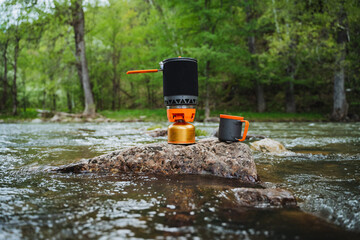 A stove sits precariously on a rock in the river, surrounded by flowing water and the beauty of...