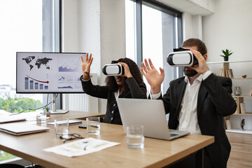 Business professionals using virtual reality headsets during meeting in modern office setting. Diverse team exploring VR technology to analyze data and visual representations on screen.