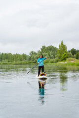 A tranquil scene of a woman paddle boarding in a lake under a cloudy sky, surrounded by boats and trees. The watercraft glides peacefully on the serene water, creating a calming setting