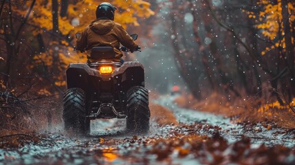 A person in a yellow jacket rides an all-terrain vehicle through a muddy forest path covered in autumn leaves, with light rain creating a picturesque scene of adventure and wilderness.