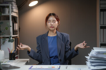 Businesswoman practicing meditation at her desk to relieve stress between workload moments in a...
