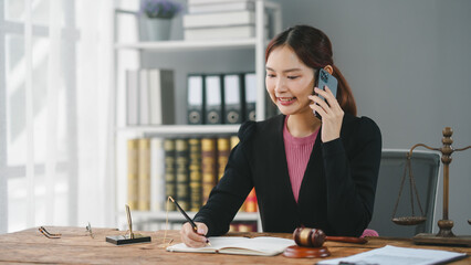 Businesswoman talking on phone and taking notes in office with bookshelf. Professional legal and administrative work environment.