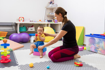 Physiotherapist helping young toddler during motor skills development exercise in rehab clinic. Early childhood intervention with physical therapy