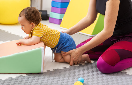 Physical therapist assisting baby with coordination exercise in rehab center for recovery after birth trauma and damage to CNS. Child rehabilitation