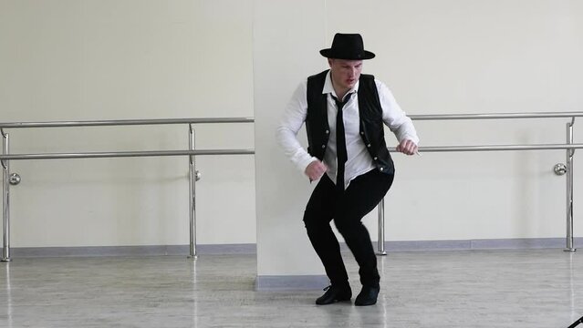 Rhythmic dance cha cha or bachata. Handsome young dancer in creative jazz clothes. Street Dancer in a hat with a tie and a black vest and jazz shoes, against the background of a wall