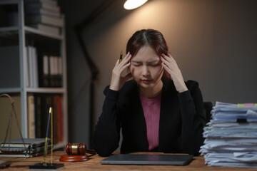 Stressed professional female lawyer working late at night in office, dealing with paperwork and legal documents.