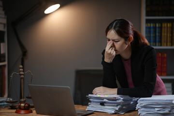 Stressed woman working late at the office, overwhelmed with documents, facing a laptop under a desk lamp. Concept of stress and workloads.