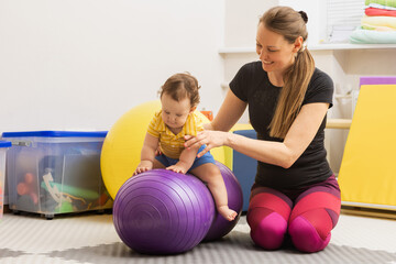 Male child with movement disorders engages in rehabilitation therapy with specialist at children's rehab center using a fitness ball to restore balance