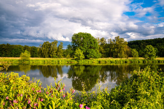 Ruhr River panorama near Schwerte Germany. Colorful evening atmosphere in springtime on the shore of calm reflecting water of a barrage. Sunlit idyllic scenery with trees after a may thunderstorm.