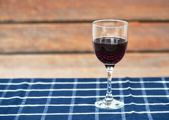 Glass of delicious red wine and ripe grapes on a checkered blue table close in the summer cottage garden.  Red natural wine, bunch of grapes in a garden in nature.